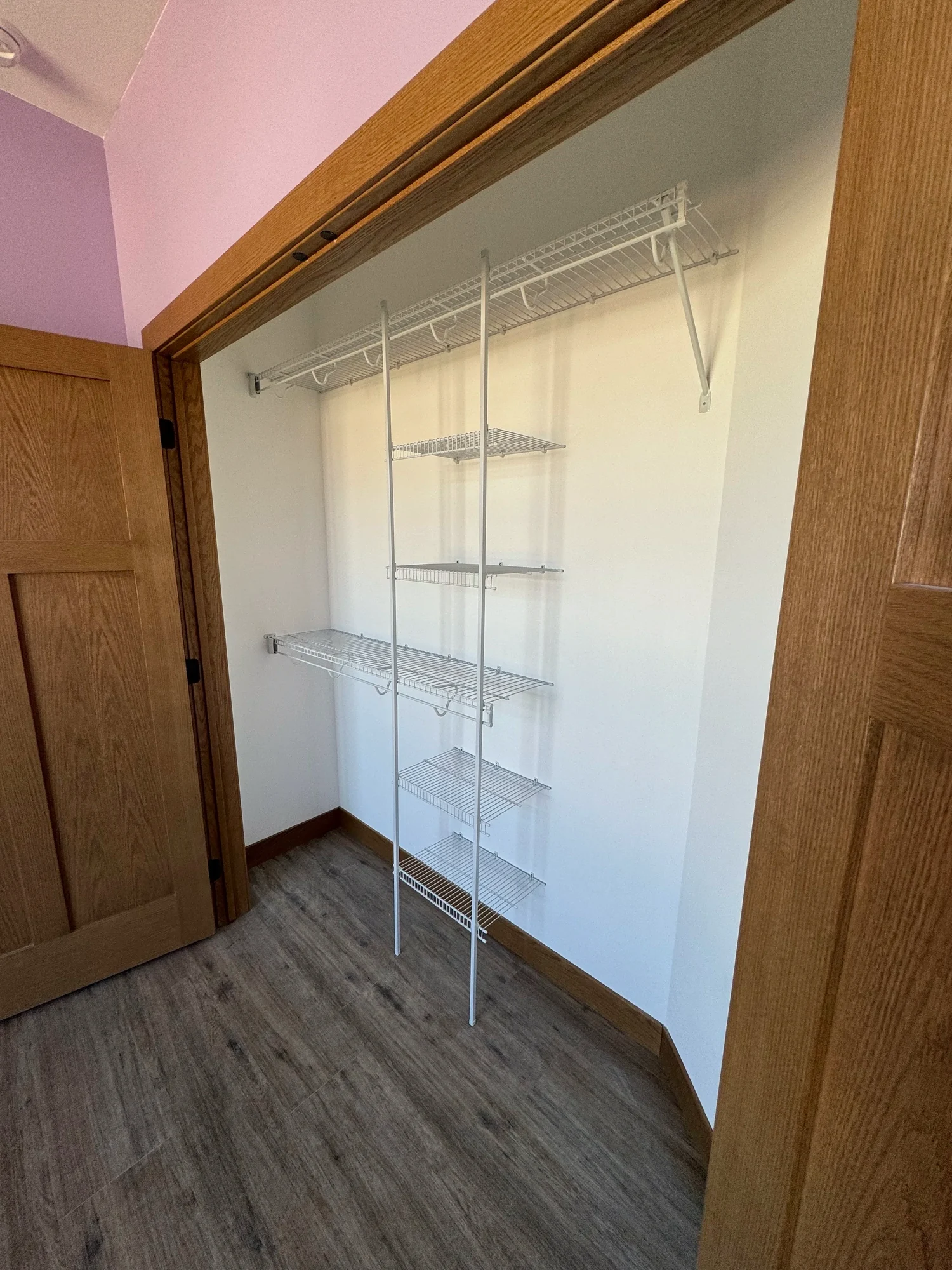 A walk-in closet behind open oak double doors, with wire shelves and a shelf tower
