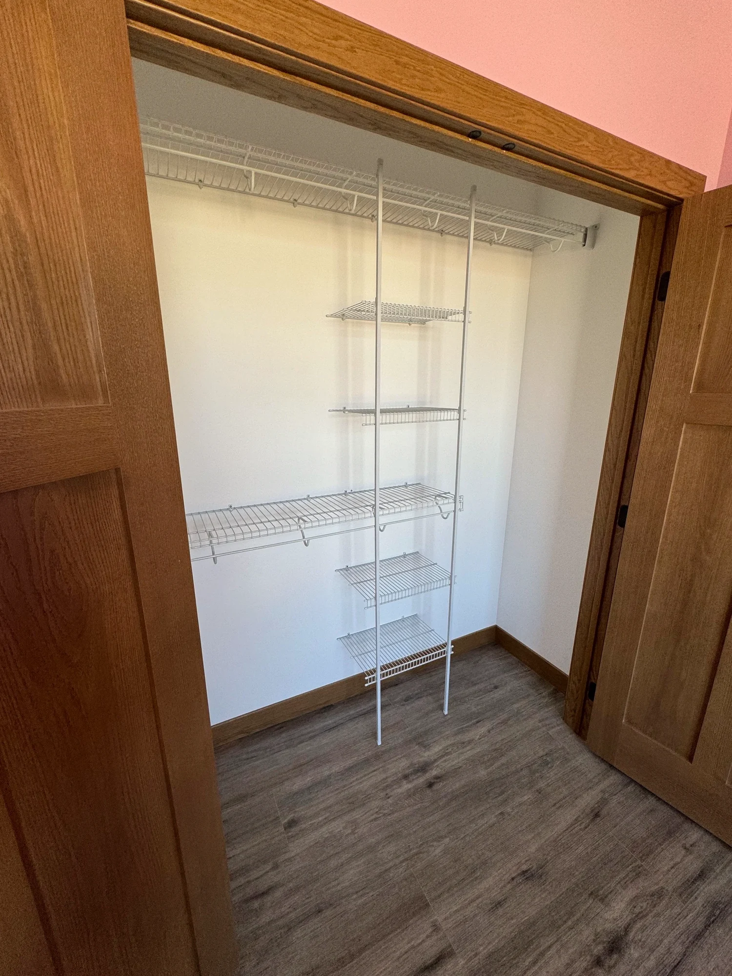 Wire shelves and a shelf tower inside a walk-in closet with oak doors