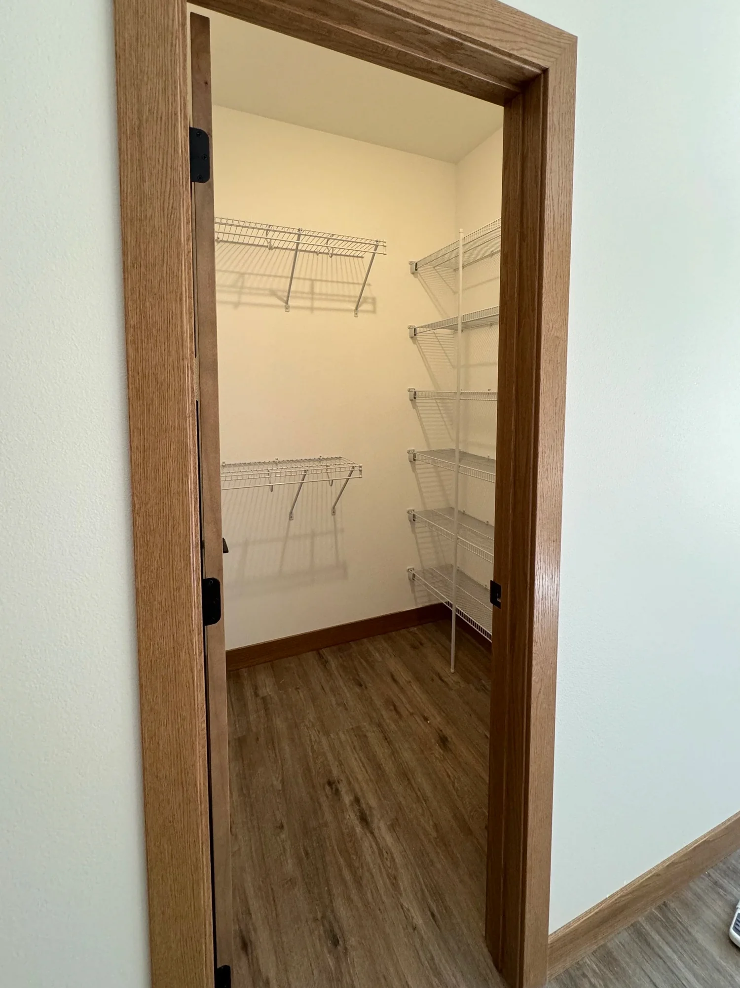 A walk-in closet with wire shelving on two walls, seen through an oak-trimmed doorway