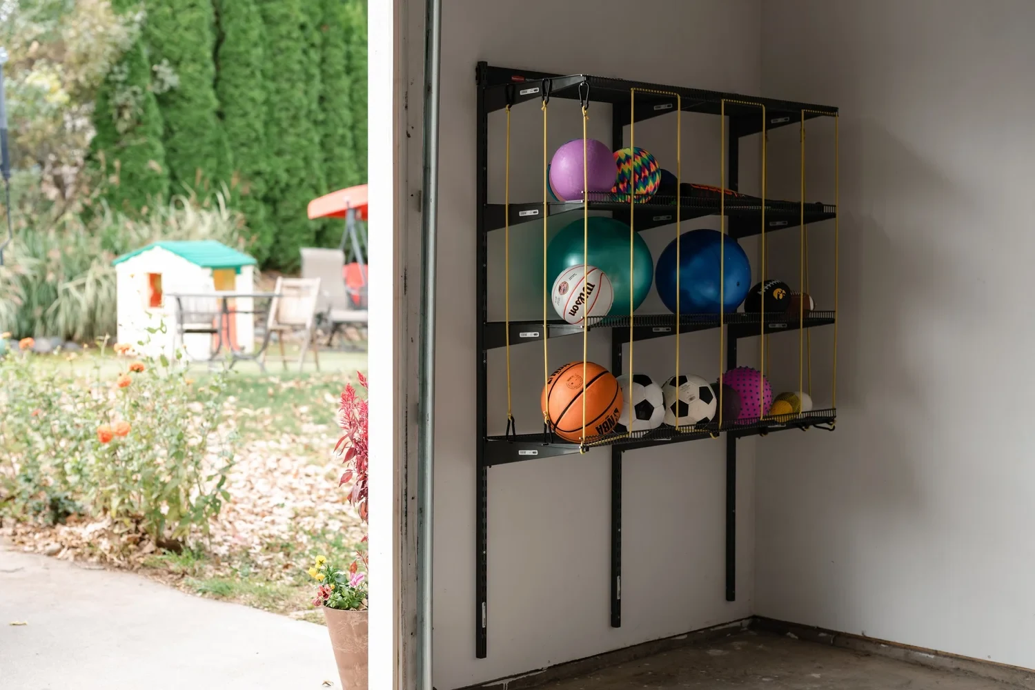 Ball storage on garage wall rails beside an open door to a backyard