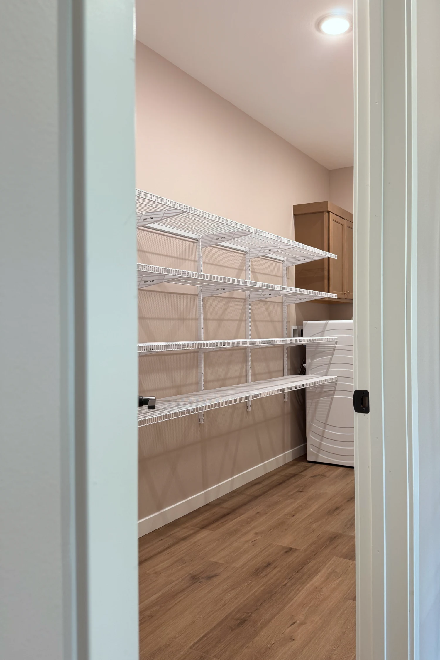 A laundry room seen through a doorway, with white wire shelves on adjustable wall standards