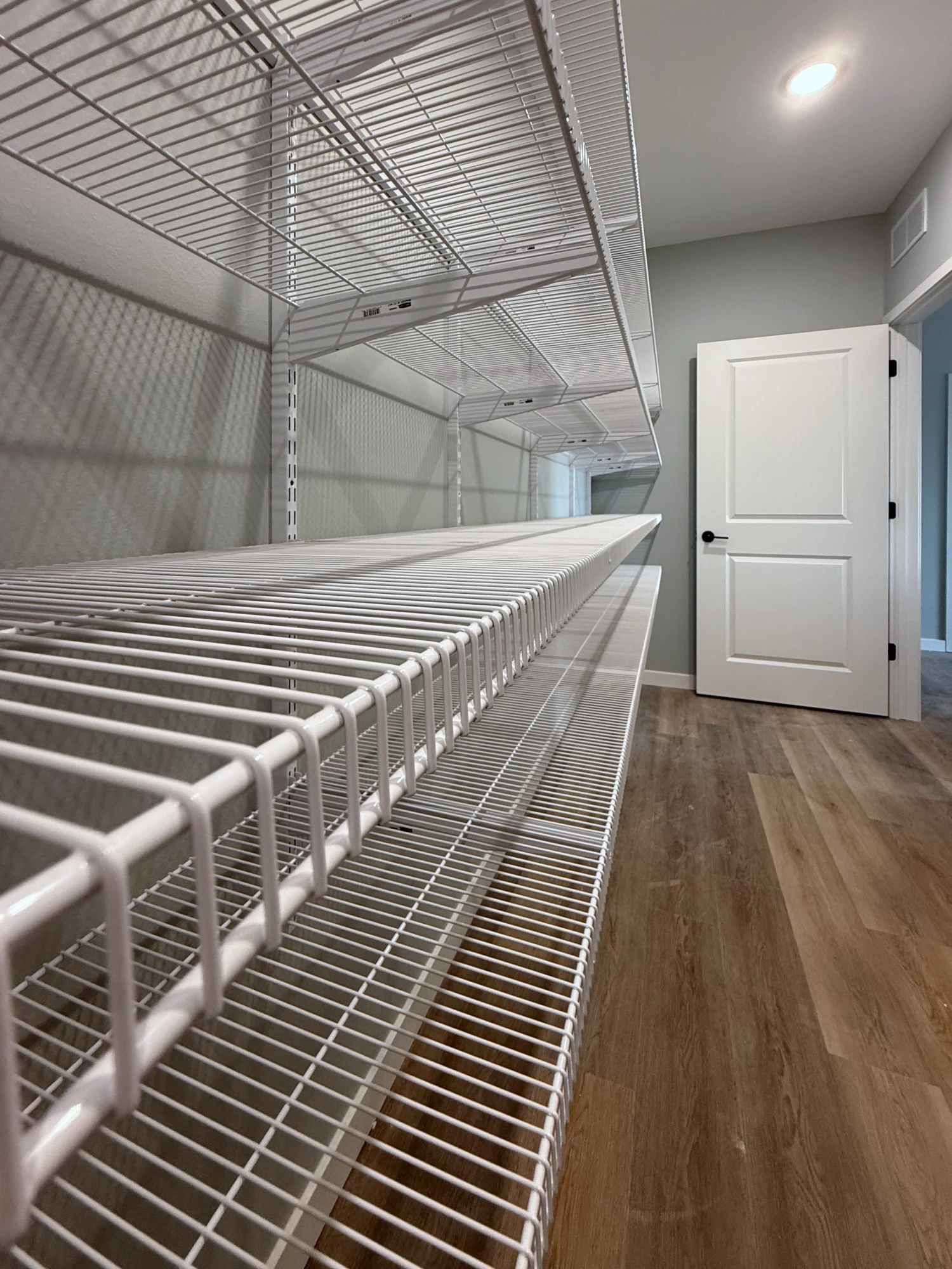 Long runs of white wire shelves on adjustable wall standards in a walk-in pantry