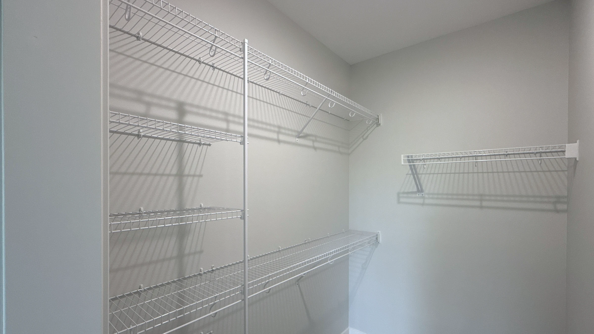 Finished walk-in closet with white wire shelving along two walls