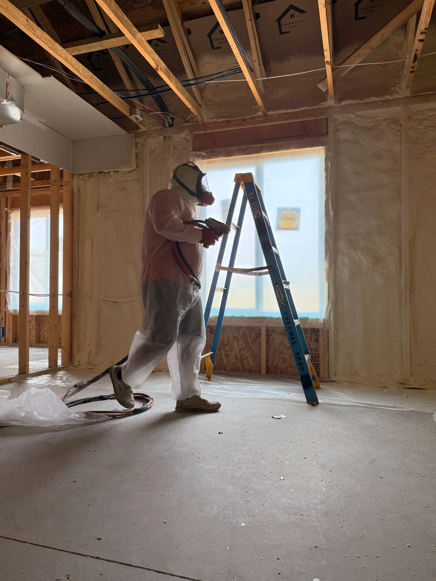 Installer spraying foam into open wall cavities beside a protected window