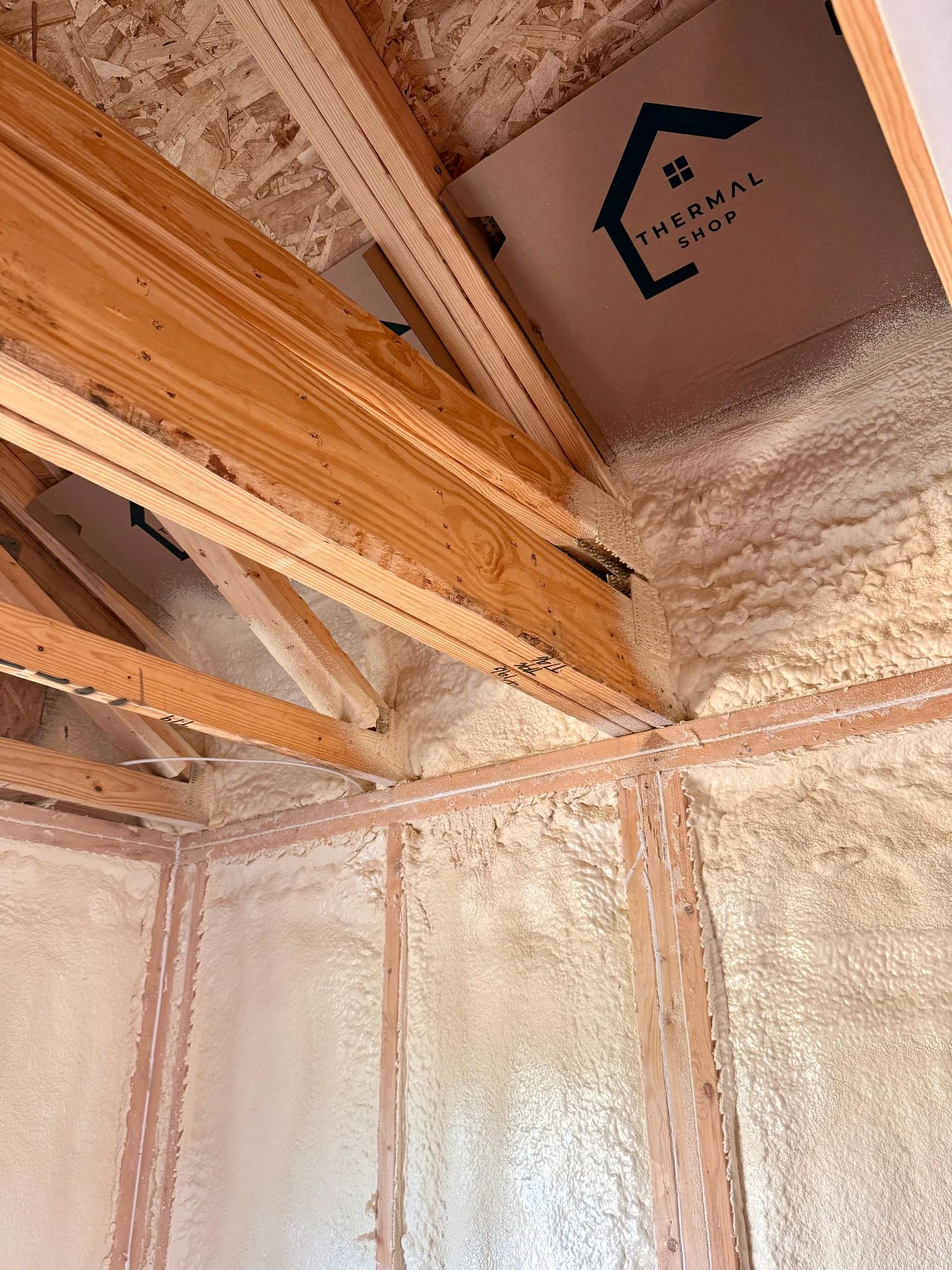 Spray foam sealing the joint where the rafters meet the top plate, with a Thermal Shop box set against the roof deck